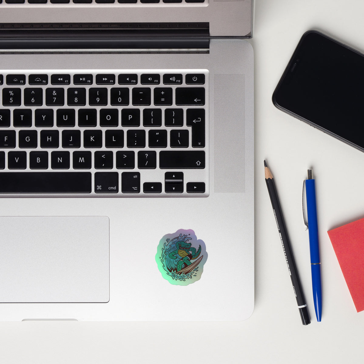 Laptop with smartphone, pen, and sticky notes on a white surface